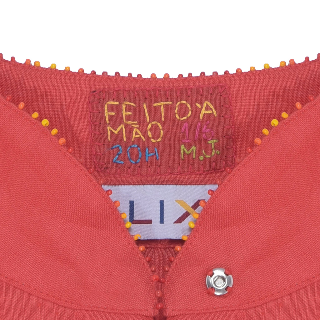 Detalhe da gola e etiqueta “Feito à Mão” do Vestido Yas Conchas, destacando o acabamento artesanal em linho coral.