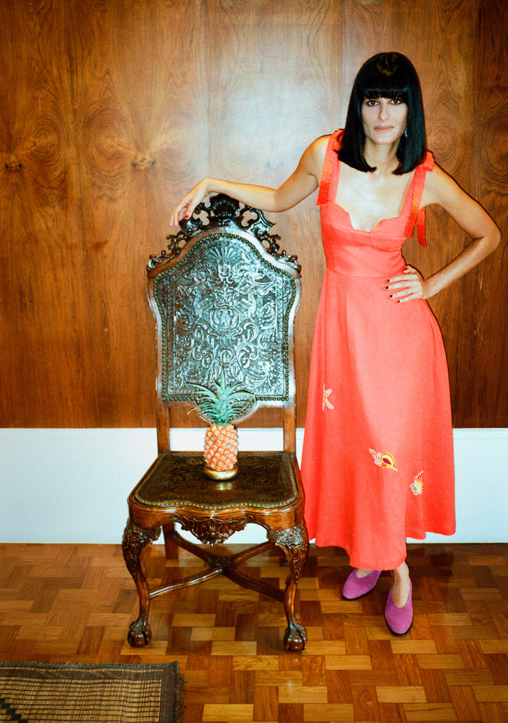 Modelo usando o vestido Betina Conchas em linho coral com bordado artesanal em miçangas multicoloridas e alças ajustáveis.