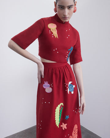 Modelo usando o Top 'Nadia' Mar da Alix em linho vermelho com bordados coloridos. Peça feminina com gola alta e fit justo.